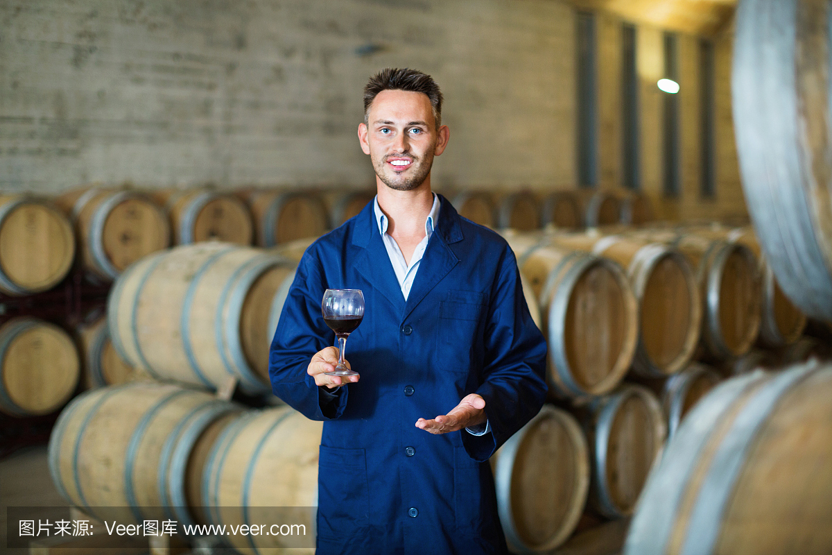 穿著制服的男釀酒師手里拿著酒杯在酒窖里